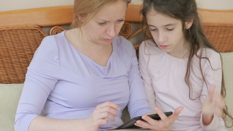 Eine schöne Mutter und ihr kleines Tochtergespräch gut, die Mutter hält eine Tablette und unterrichtet ihre Tochter