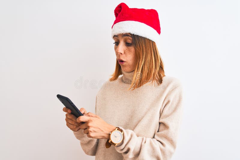Eine schöne Rothoutiquin mit Weihnachtsmütze und Smartphone, erschreckt mit Überraschungsangst und begeistert von stockfotografie