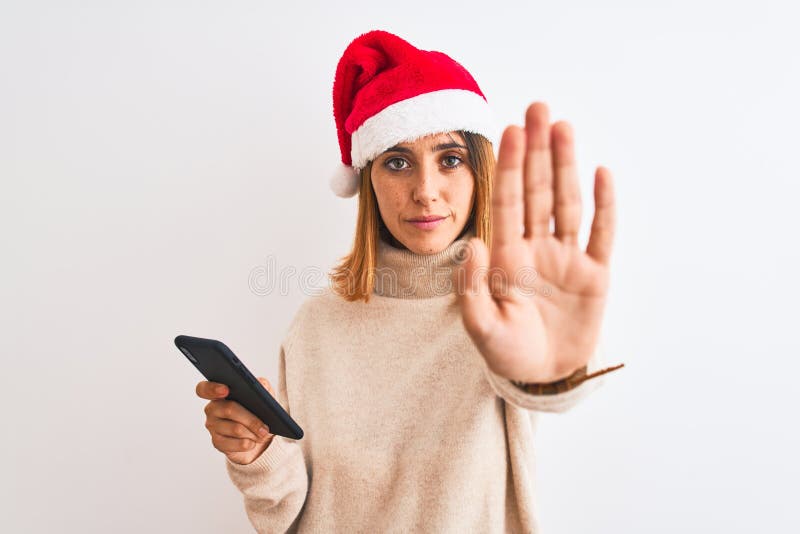 Eine schöne Rotkopffrau, die Weihnachtsmütze trägt und ein Smartphone mit offener Hand benutzt, um ein Stoppschild mit ernster und stockfotografie