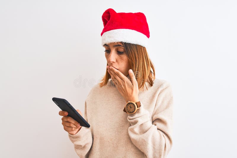 Eine schöne Rotkopffrau, die Weihnachtsmütze trägt und mit einem Handtuchdeckel den Mund nimmt, der mit der Hand geschockt wurde lizenzfreies stockfoto