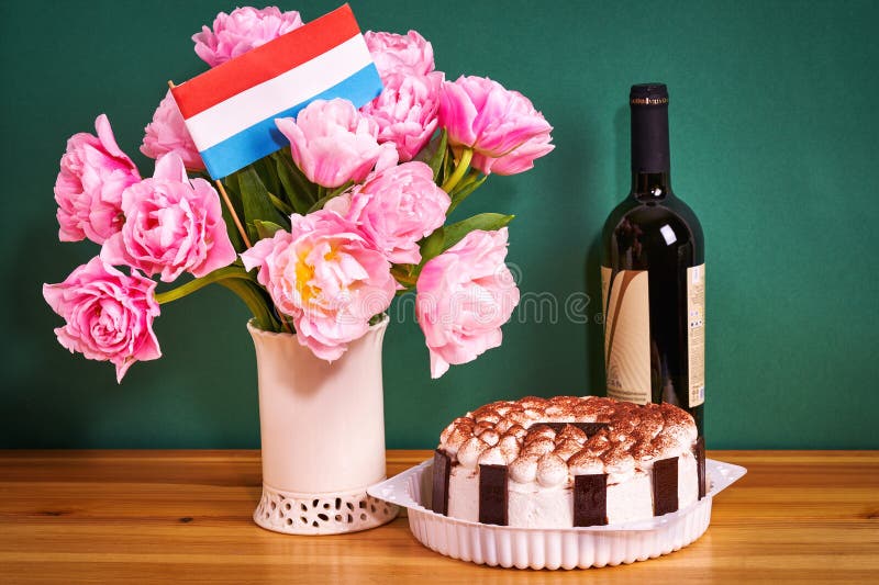Eine Tulpe eine Flasche Wein, ein köstlicher Kuchen und die niederländische Flagge auf einem Holztisch stockfoto