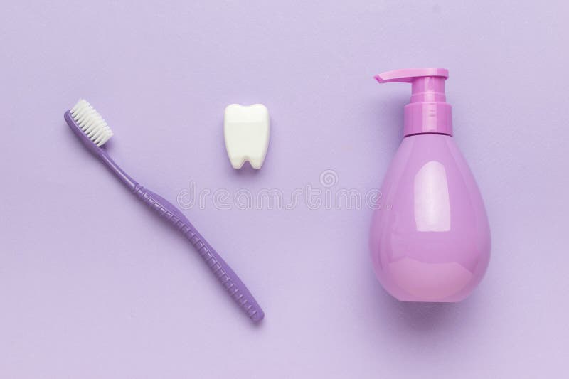 Eine violette Zahnbürste, eine originale Zahnpasteurröhre und eine Zahnfigur auf violettem Hintergrund lizenzfreies stockbild
