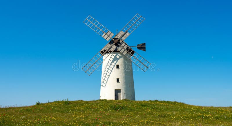 Eine weiße, traditionelle Windmühle mit einem kegelförmigen Turm und vier großen Latticestyle-Segel stock abbildung