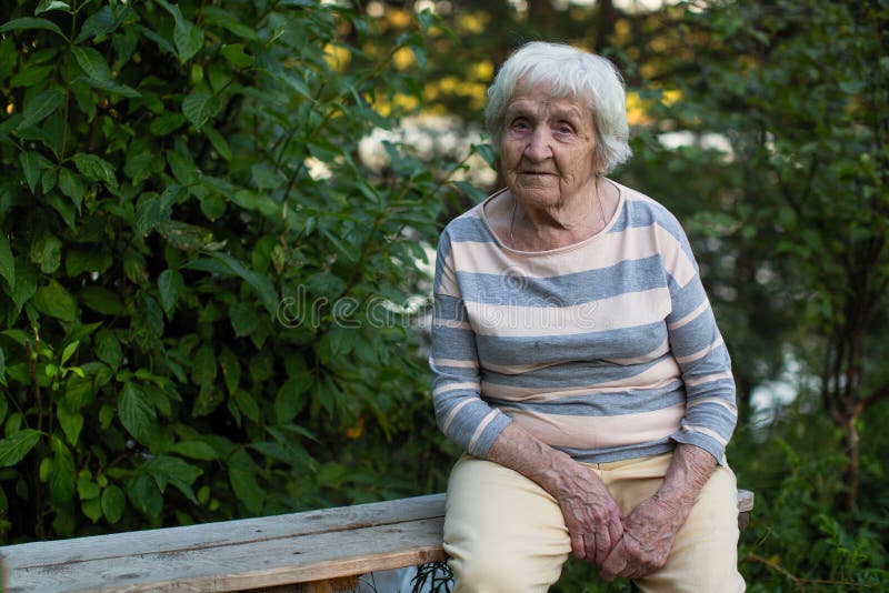 Eine ältere einzige Frau, die auf einer Holzbank im Park sitzt stockfotografie Eine ältere einzige Frau, die auf einer Holzbank im Park sitzt stockfotografie