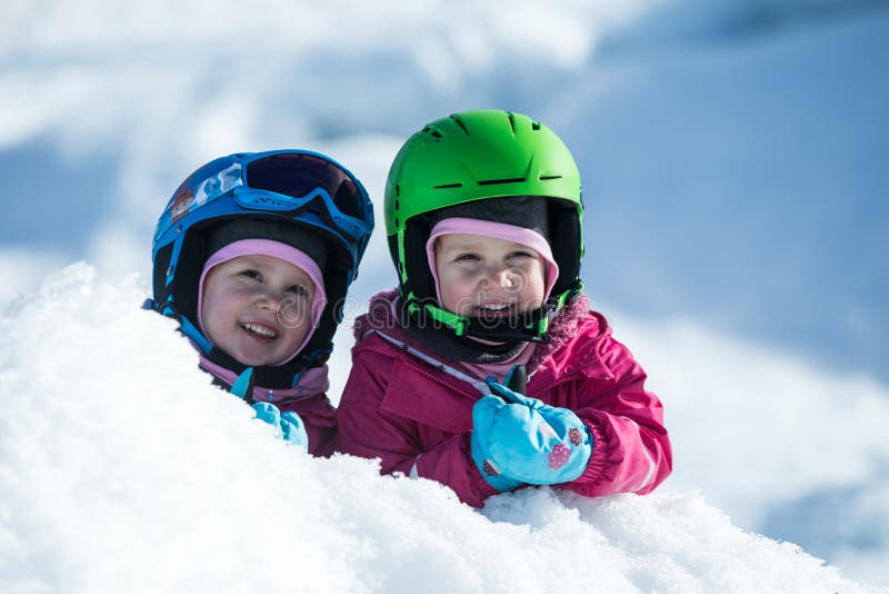 Identical twins are having fun in snow. Kids with safety helmet. Winter sport for family. Little kids outside, swiss Alps, mountains, healthy lifestyle, cheerful family, smiling cute girls. Identical twins are having fun in snow. Kids with safety helmet. Winter sport for family. Little kids outside, swiss Alps, mountains, healthy lifestyle, cheerful family, smiling cute girls