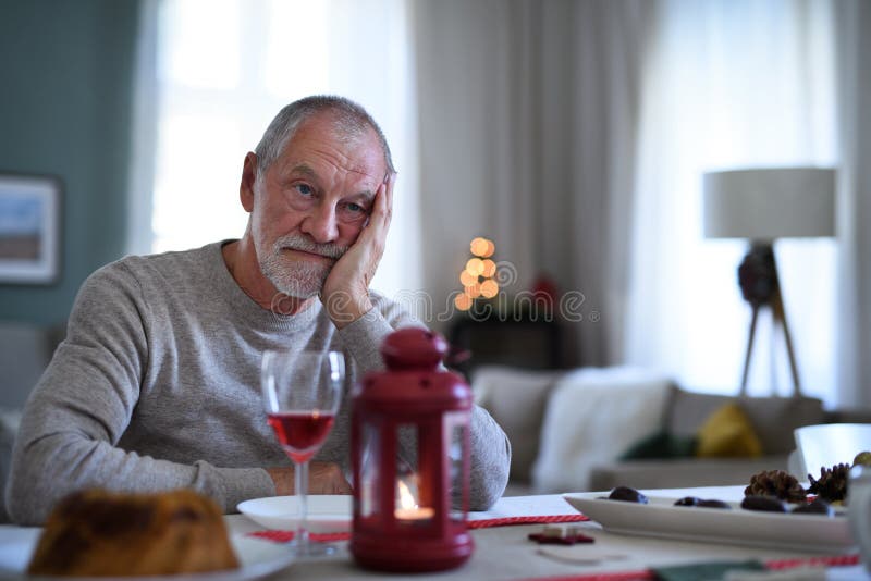 Einsamer älterer Mann mit dem Wein, der in Innenräumen am Tisch zu Weihnachten Einsamkeitskonzept sitzt.
