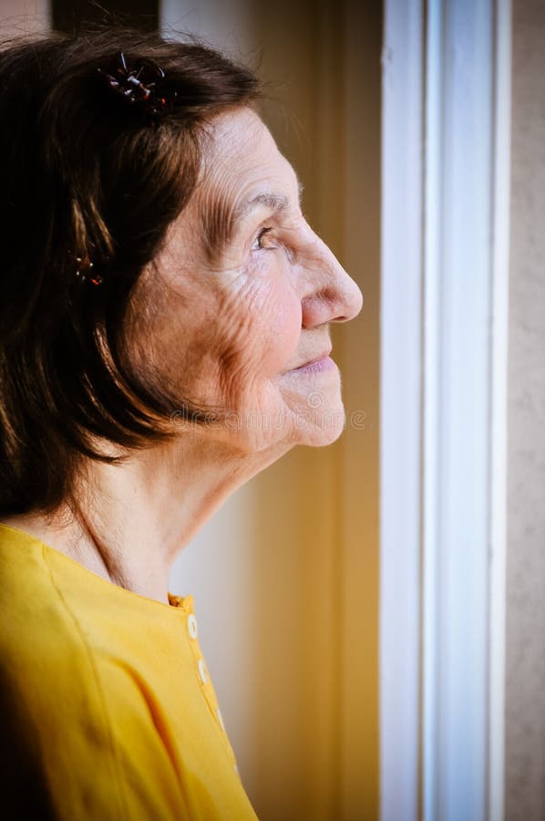 Einsamkeit - ältere Frau, die durch Fenster schaut