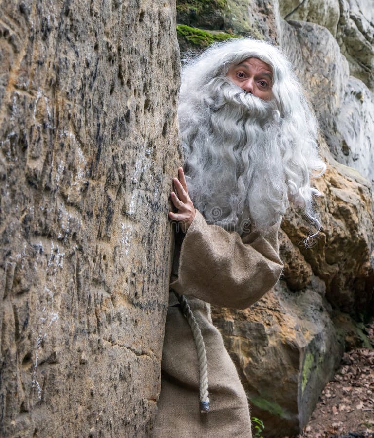 Surprised hermit peeks behind rock. The bearded monk in nature. Surprised hermit peeks behind rock. The bearded monk in nature.