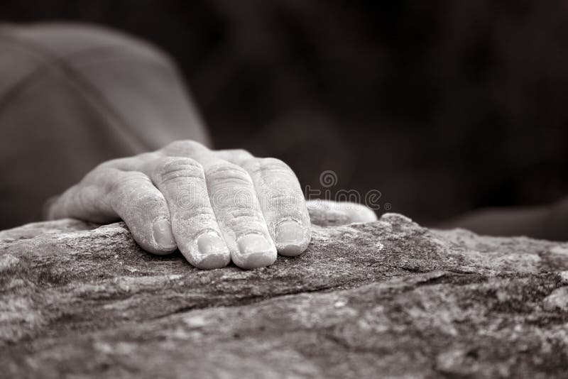 A lonely hand holding onto the top of a rock as a climber reaches the peak. This image has a slight sepia tone to it. A lonely hand holding onto the top of a rock as a climber reaches the peak. This image has a slight sepia tone to it.