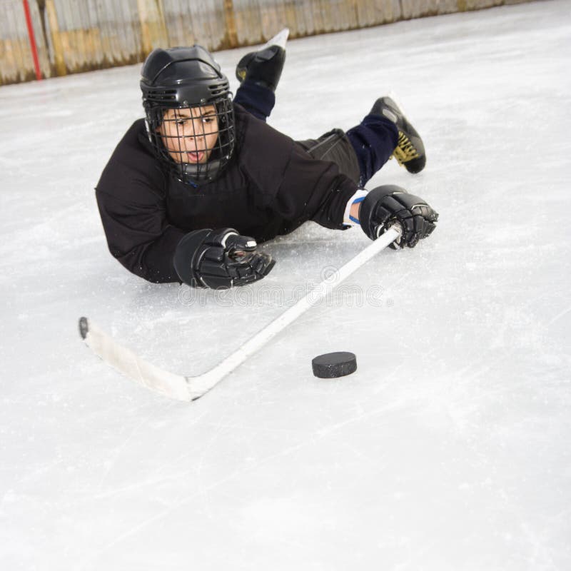 Ice hockey player boy in uniform sliding on ice holding stick out towards puck. Ice hockey player boy in uniform sliding on ice holding stick out towards puck.