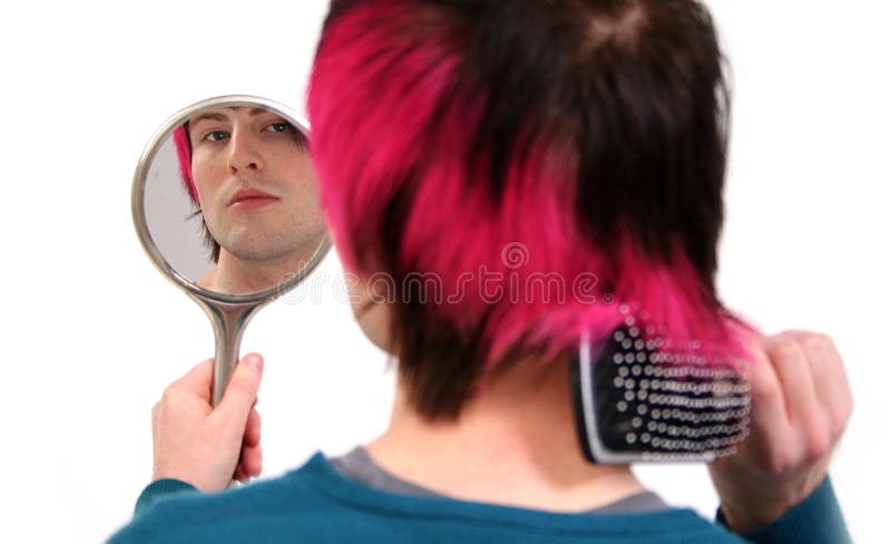 Brush hair and grooming. Teenager or young adult styling his hair whilst looking in mirror. Gay or metrosexual guy with black and pink or purple hair comb with hair brush. Brush hair and grooming. Teenager or young adult styling his hair whilst looking in mirror. Gay or metrosexual guy with black and pink or purple hair comb with hair brush.