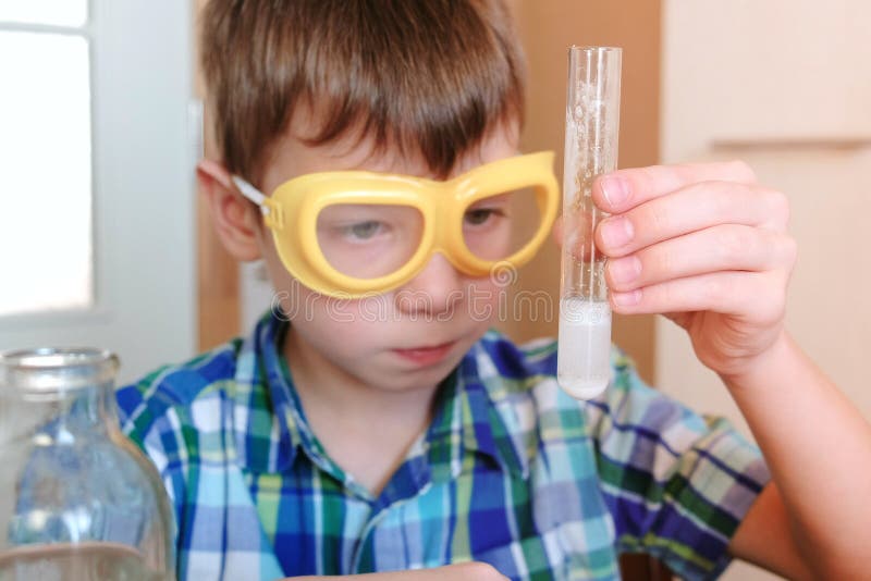 Eksperymenty na chemii w domu Chłopiec jest przyglądającym Chemicznym reakcją z uwolnieniem gaz w próbnej tubce w rękach obrazy stock Eksperymenty na chemii w domu Chłopiec jest przyglądającym Chemicznym reakcją z uwolnieniem gaz w próbnej tubce w rękach obrazy stock