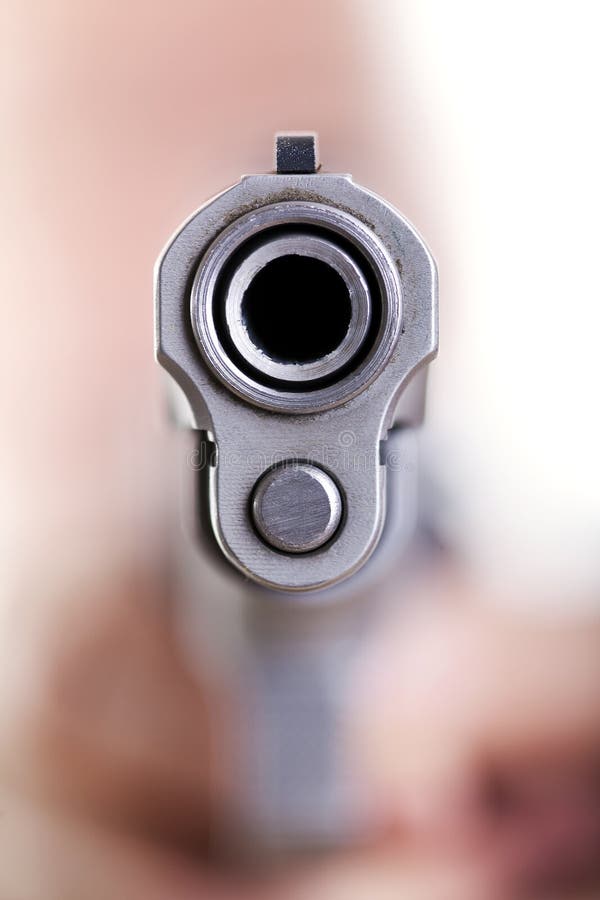 Extreme close up macro shot of the dangerous front edge of a 9mm handgun. Even though the depth of field is extremely shallow, an obscured shape of a head and hands holding the gun can be seen in the background, defocused. Extreme close up macro shot of the dangerous front edge of a 9mm handgun. Even though the depth of field is extremely shallow, an obscured shape of a head and hands holding the gun can be seen in the background, defocused.