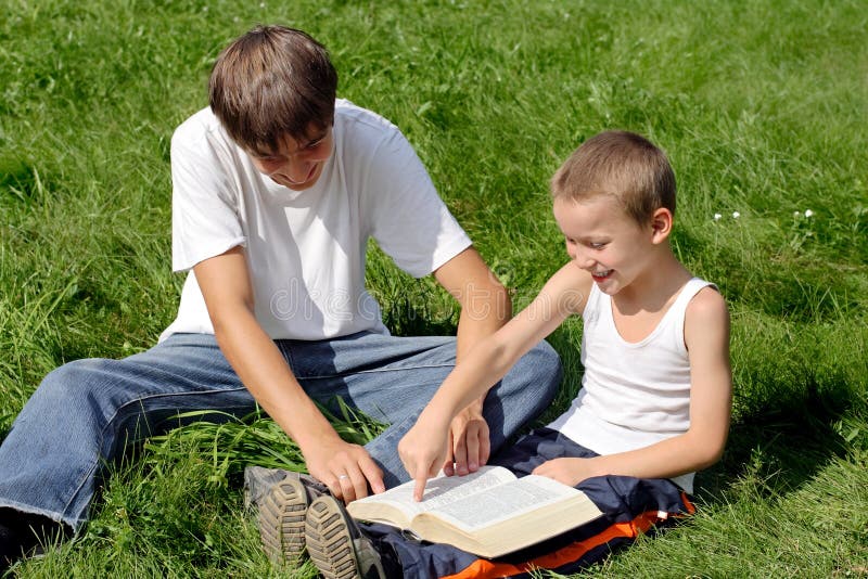 Older and Little Brothers reads a Book in the Summer Park. Older and Little Brothers reads a Book in the Summer Park