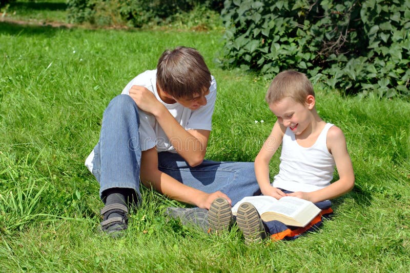 Older and Little Brothers reads a Book in the Summer Park. Older and Little Brothers reads a Book in the Summer Park