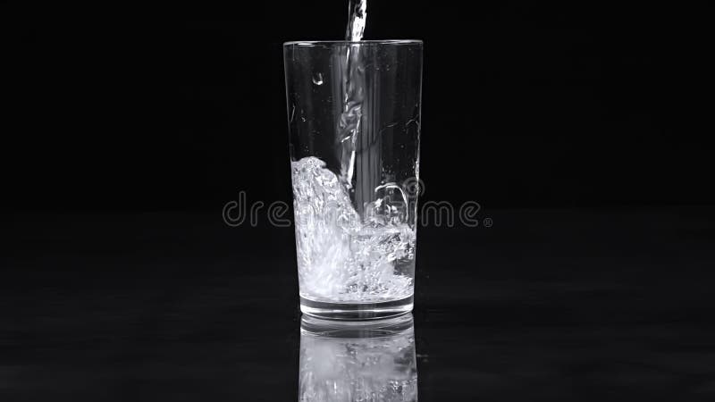 El agua se vierte en un vaso con salpicaduras en un fondo negro. movimiento lento