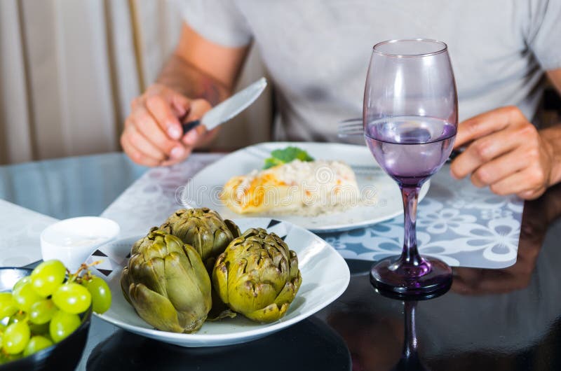 El ajuste con clase de la tabla de cena, alcachofas cocinadas que se sientan en centro, sirve los cubiertos que se sostienen visi fotos de archivo El ajuste con clase de la tabla de cena, alcachofas cocinadas que se sientan en centro, sirve los cubiertos que se sostienen visi fotos de archivo