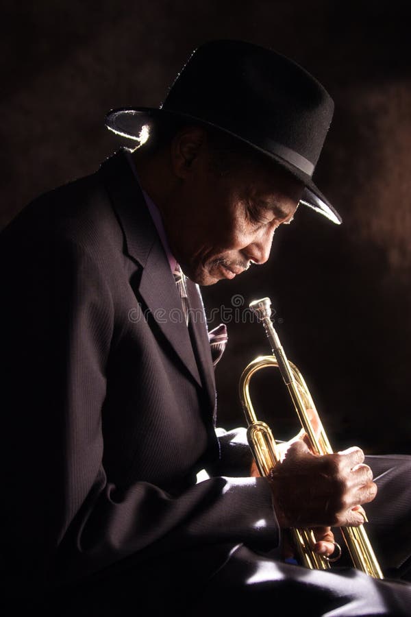 A stock image of an elderly black man in a suit holding an old horn with a look of sadness. A stock image of an elderly black man in a suit holding an old horn with a look of sadness.