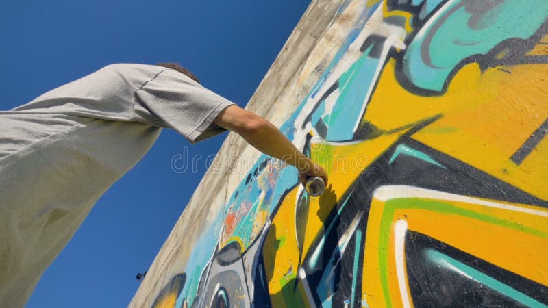 El artista de la pintada está pintando una letra amarilla en la pared, visión de debajo