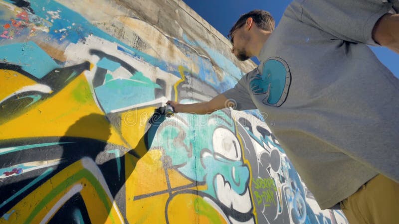 El artista de la pintada está pintando una letra amarilla en la pared, visión desde el lado izquierdo, de debajo