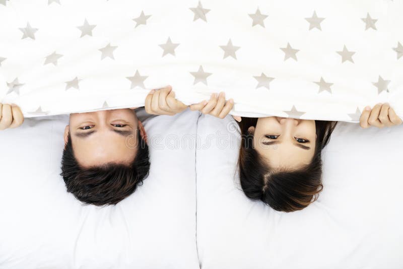 El asiático casó a la pareja que mentía y que ocultaba debajo de la cama combinada de las estrellas blancas que miraba la cámara imagen de archivo libre de regalías El asiático casó a la pareja que mentía y que ocultaba debajo de la cama combinada de las estrellas blancas que miraba la cámara imagen de archivo libre de regalías