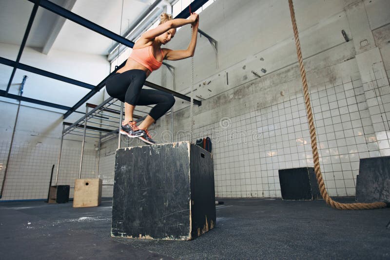 El atleta de sexo femenino está realizando saltos de la caja en el gimnasio