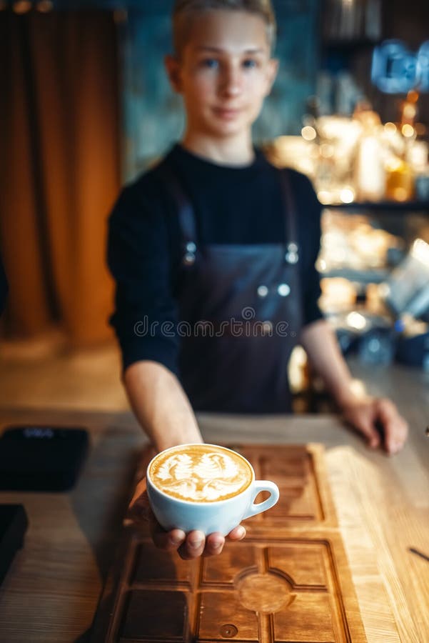 El barista masculino muestra la taza de café con el dibujo de la espuma fotografía de archivo libre de regalías El barista masculino muestra la taza de café con el dibujo de la espuma fotografía de archivo libre de regalías