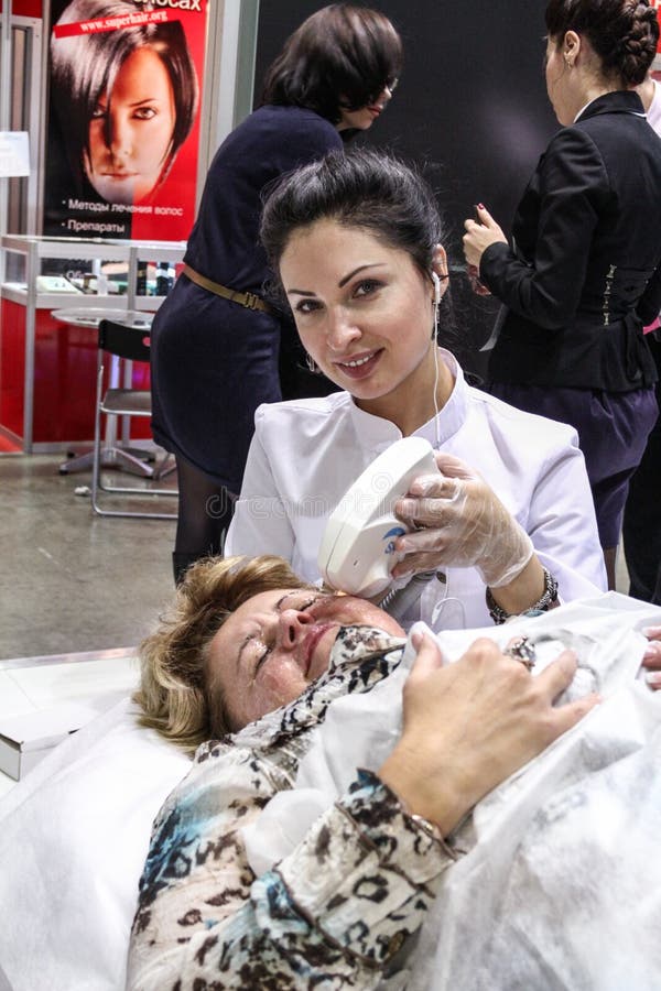 MOSCOW - OCTOBER 26: Beautician performs a laser procedure at the international exhibition of professional cosmetics and beauty salon equipment INTERCHARM on October 26, 2011 in Moscow. MOSCOW - OCTOBER 26: Beautician performs a laser procedure at the international exhibition of professional cosmetics and beauty salon equipment INTERCHARM on October 26, 2011 in Moscow