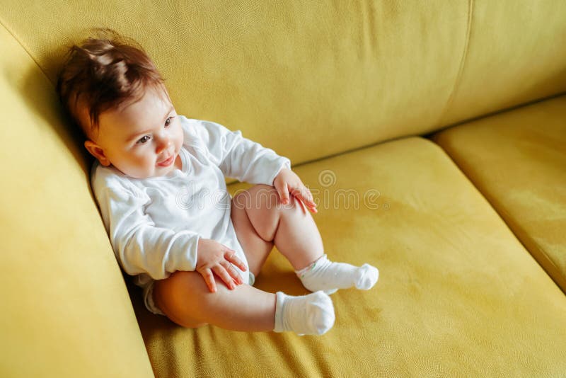 El Bebé Está Sentado En El Sofá Amarillo En Casa. Foto de archivo