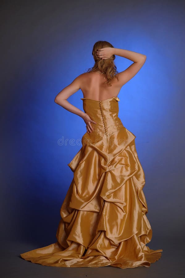 El Blonde en un vestido elegante del oro está detrás en la imagen foto de archivo libre de regalías El Blonde en un vestido elegante del oro está detrás en la imagen foto de archivo libre de regalías