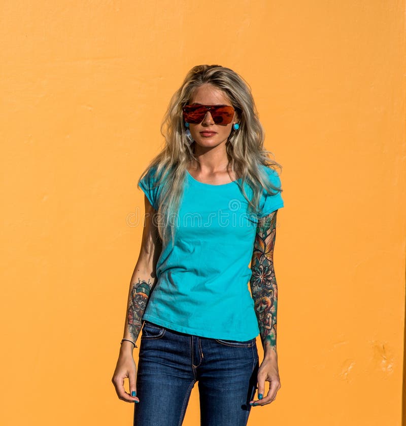El blonde hermoso en gafas de sol mira la cámara Retrato en el fondo de la pared anaranjada brillante Muchacha moderna del inconf fotos de archivo El blonde hermoso en gafas de sol mira la cámara Retrato en el fondo de la pared anaranjada brillante Muchacha moderna del inconf fotos de archivo