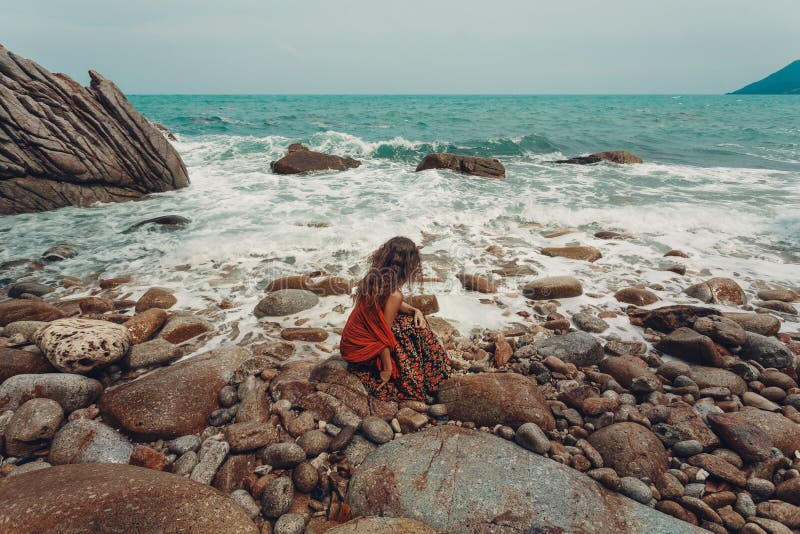 El boho joven hermoso diseñó a la mujer que se sentaba en una playa de piedra fotografía de archivo