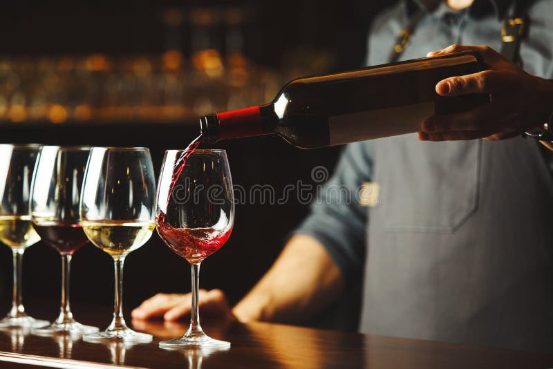 El camarero vierte el vino rojo en vidrios en contador de madera de la barra imágenes de archivo libres de regalías El camarero vierte el vino rojo en vidrios en contador de madera de la barra imágenes de archivo libres de regalías