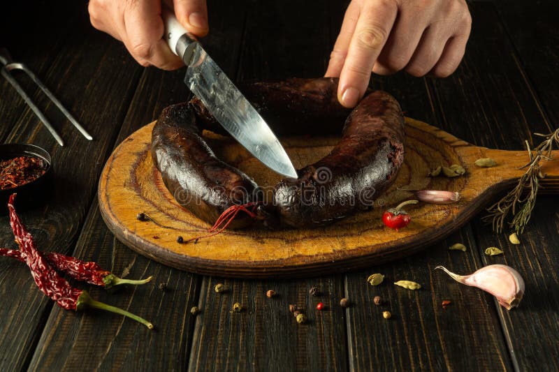 El chef elabora un plato nacional con especias y pimienta en casa. salchichas de sangre cortadas por las manos del cocinero con un fotografía de archivo libre de regalías