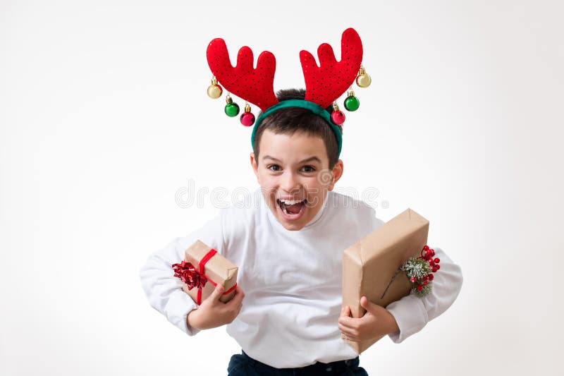 El chico con un aro en forma de astas de ciervo en la cabeza doblada sobre con regalos en sus manos. Concepto de Navidad fotografía de archivo