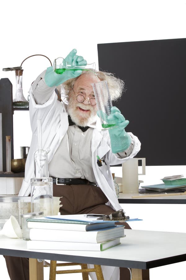 Cheerful mad senior scientist in lab measures green liquid in beaker. Frizzy grey hair, round glasses, lab coat, geek trousers, aqua rubber gloves, blank blackboard, vertical, high key, copy space. Cheerful mad senior scientist in lab measures green liquid in beaker. Frizzy grey hair, round glasses, lab coat, geek trousers, aqua rubber gloves, blank blackboard, vertical, high key, copy space.