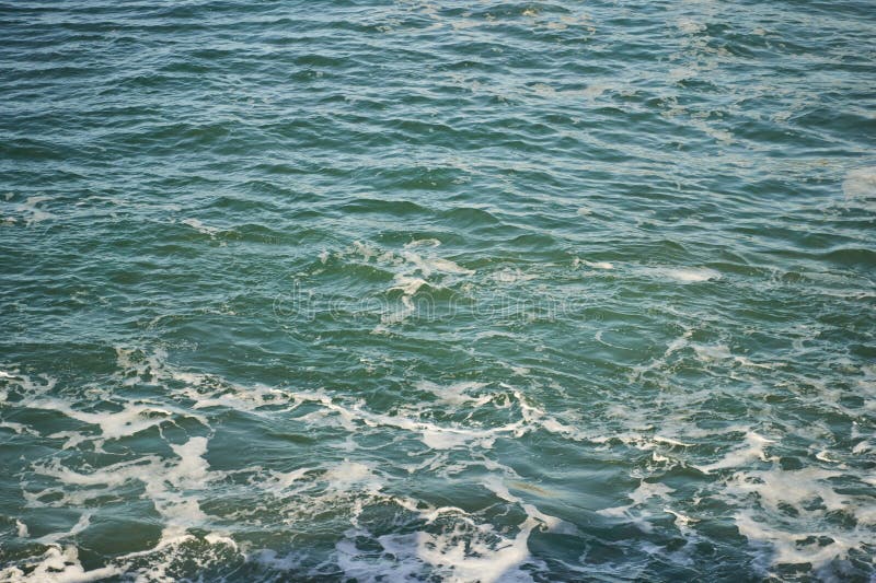 El cierre de un cuerpo de agua con olas estrellándose en la orilla. Una captura de pantalla del océano con olas de viento que caen sobre la orilla creando un hermoso patrón de peleas en el agua. el paisaje se ve reforzado por las nubes de los cumulus en el cielo