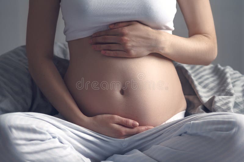 El cierre frontal para arriba del matón de la mujer embarazada en abrazos de la cama tiraniza el paso de un héroe, yoga prenatal imagen de archivo El cierre frontal para arriba del matón de la mujer embarazada en abrazos de la cama tiraniza el paso de un héroe, yoga prenatal imagen de archivo