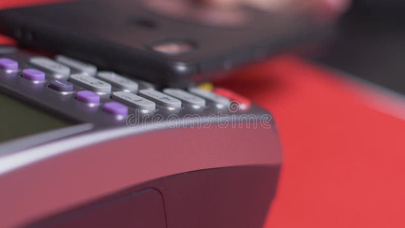 El cliente paga con un teléfono negro a través de un terminal gris que se coloca metrajes