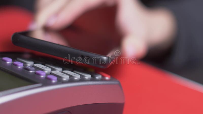 El cliente paga con un teléfono negro a través de un terminal gris que se coloca metrajes