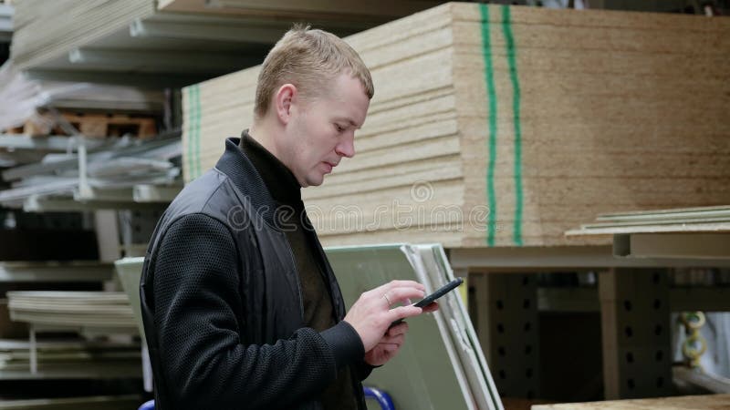 El cliente se involucra con un smartphone que compara los precios y las revisiones de lectura mientras selecciona materiales de co almacen de metraje de vídeo