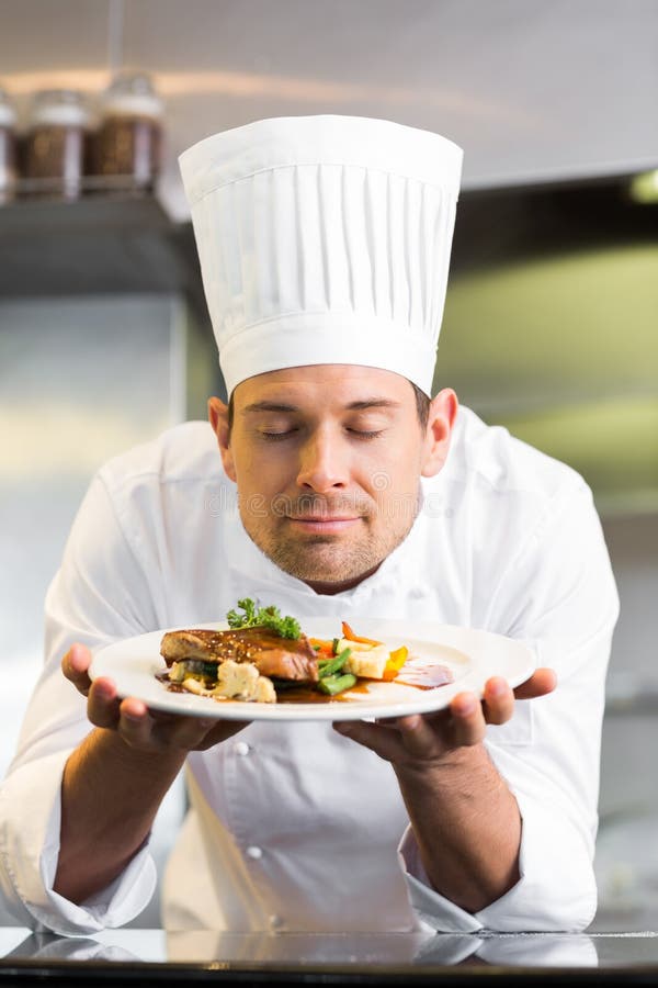 El cocinero de sexo masculino con los ojos cerró la comida que olía en cocina imagen de archivo El cocinero de sexo masculino con los ojos cerró la comida que olía en cocina imagen de archivo