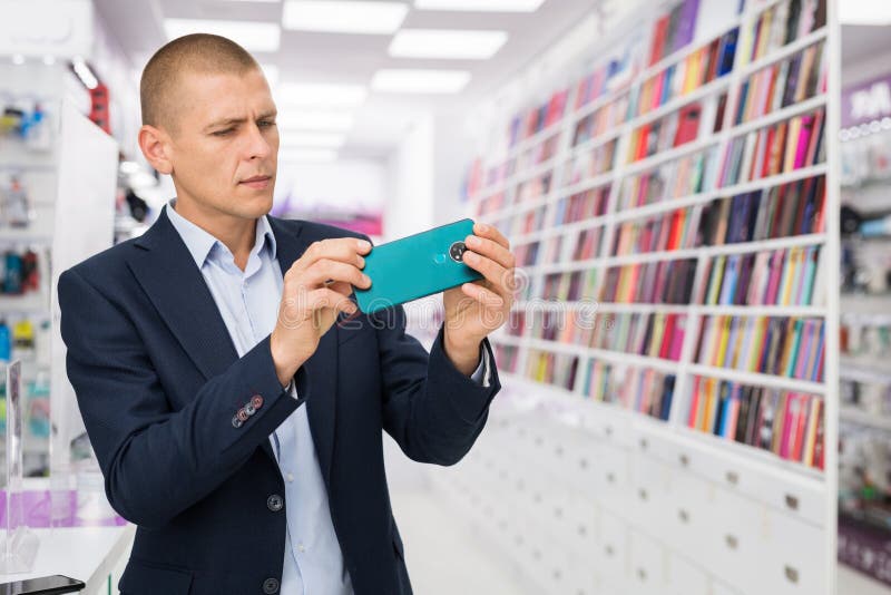 Smiling elegant young man standing in tech store with new smart phone in his hands. Smiling elegant young man standing in tech store with new smart phone in his hands