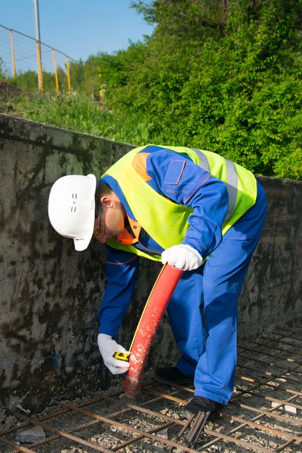 El constructor mide el tubo rojo para poner los cables eléctricos en parques antes de verter la fundación del camino fotos de archivo El constructor mide el tubo rojo para poner los cables eléctricos en parques antes de verter la fundación del camino fotos de archivo
