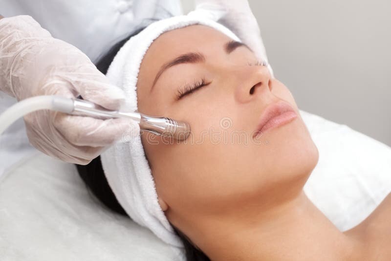 The cosmetologist makes the procedure Microdermabrasion of the facial skin of a beautiful, young woman in a beauty salon.Cosmetology and professional skin care. The cosmetologist makes the procedure Microdermabrasion of the facial skin of a beautiful, young woman in a beauty salon.Cosmetology and professional skin care.