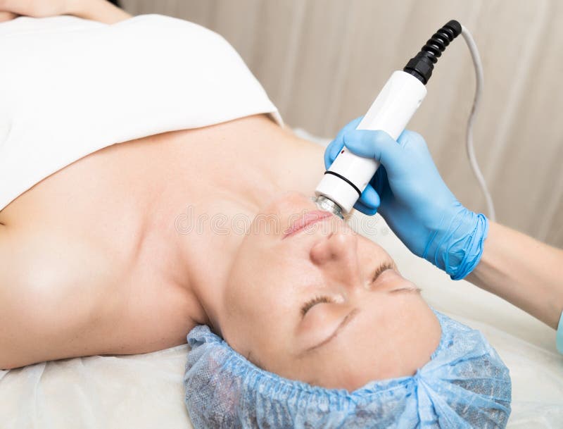 El cosmetólogo hace la RF-elevación a la mujer joven Los procedimientos cosméticos para la cara Tratamientos de la belleza en el imágenes de archivo libres de regalías El cosmetólogo hace la RF-elevación a la mujer joven Los procedimientos cosméticos para la cara Tratamientos de la belleza en el imágenes de archivo libres de regalías