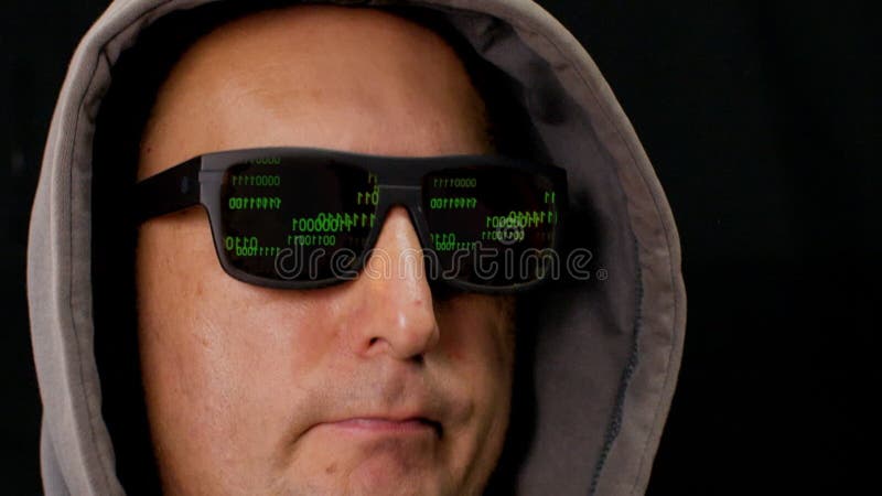El código binario verde se refleja en las gafas negras de las gafas de hackers. hacker informático con gafas negras y capucha