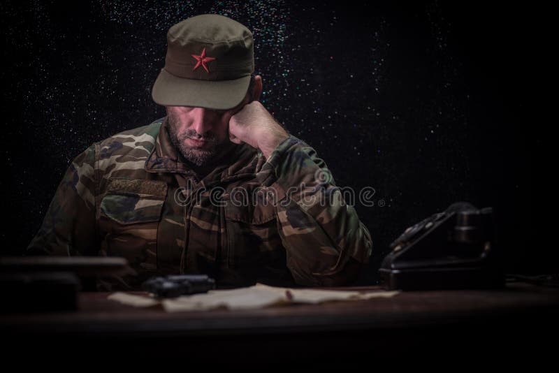 El dictador malvado que se sienta en la tabla Sentada general comunista enojada en la sede o el comandante cubano en sitio oscuro