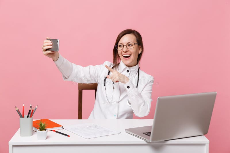 El doctor de sexo femenino se sienta en el trabajo de escritorio en el ordenador con el teléfono móvil médico del control del doc imagen de archivo libre de regalías El doctor de sexo femenino se sienta en el trabajo de escritorio en el ordenador con el teléfono móvil médico del control del doc imagen de archivo libre de regalías