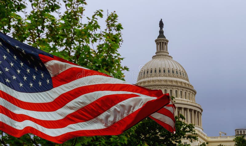 El edificio del capitolio de los E.E.U.U. con una bandera americana que agita sobrepuesta en el cielo